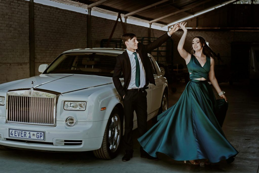 Stylish couple dancing beside a Rolls-Royce in a hangar setting, showcasing elegance and joy.