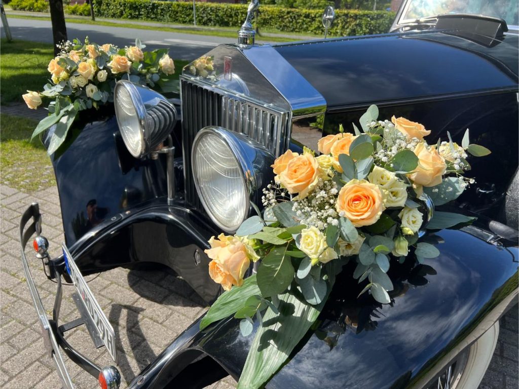 Eine Braut hebt während einer Hochzeitsfeier freudig ihren Blumenstrauß in einem Oldtimer-Cabrio hoch.